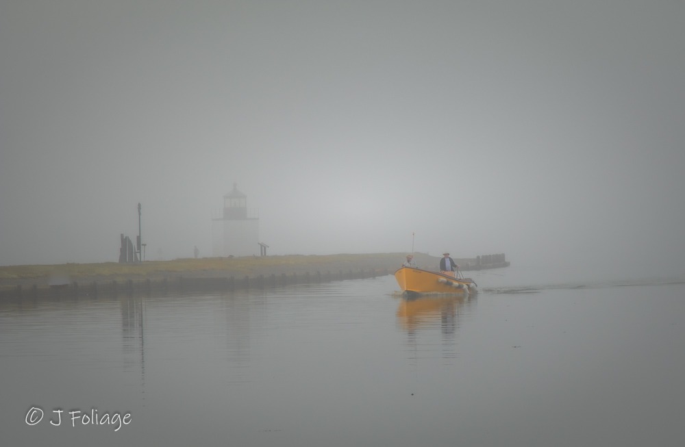 Derby Wharf Light in Salem, Massachusetts, shrouded in morning fog with a small boat reflected in the calm harbor water.