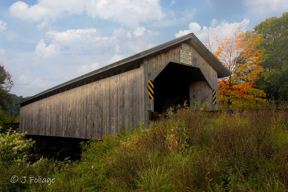 Exterior view of the Hopkins Covered Bridge in Montgomery, Vermont, surrounded by early autumn foliage