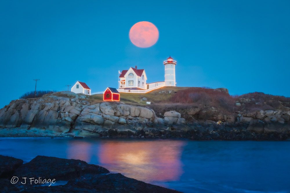Nubble Lighthouse decorated with Christmas lights under a full moon in winter. Full moon rising over Nubble Lighthouse viewed from Sohier Park Beach in York Maine