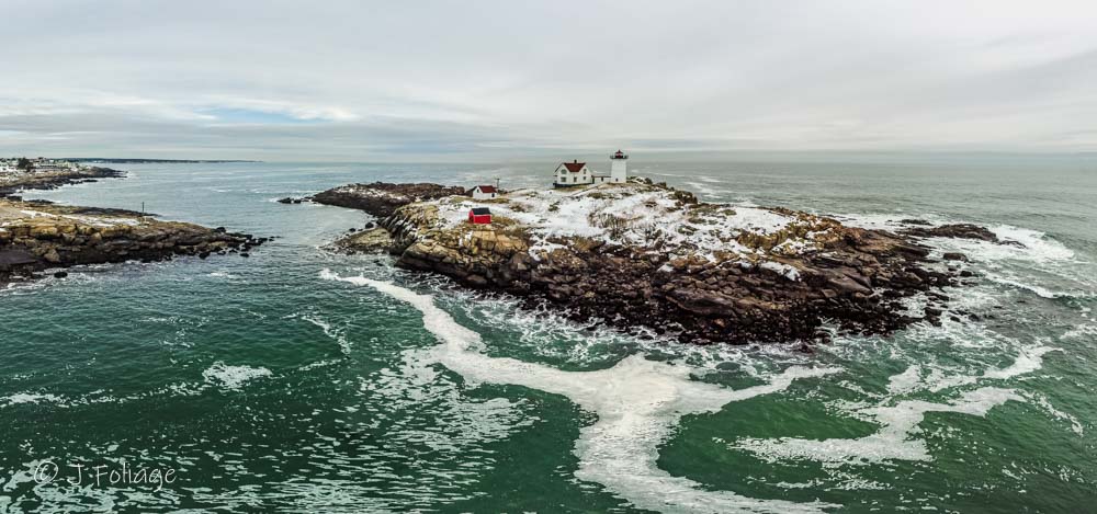 Panoramic winter landscape of Nubble Lighthouse on a rocky island in York Maine during a cold December morning.