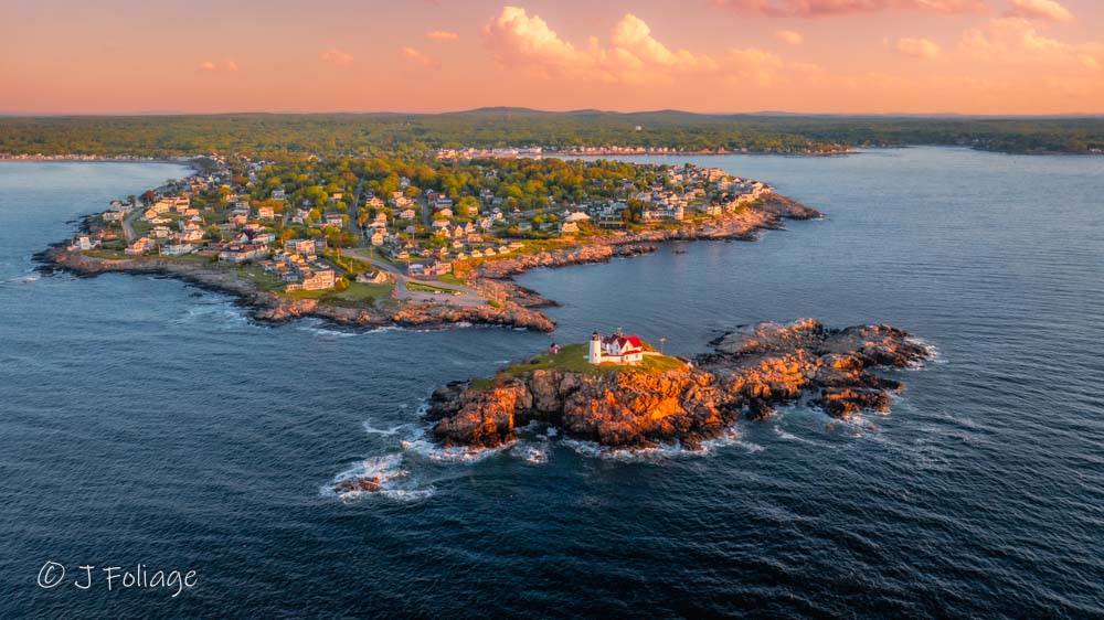 Aerial drone view of Cape Neddick Nubble Lighthouse in May showing green spring grass and blue Atlantic waters.