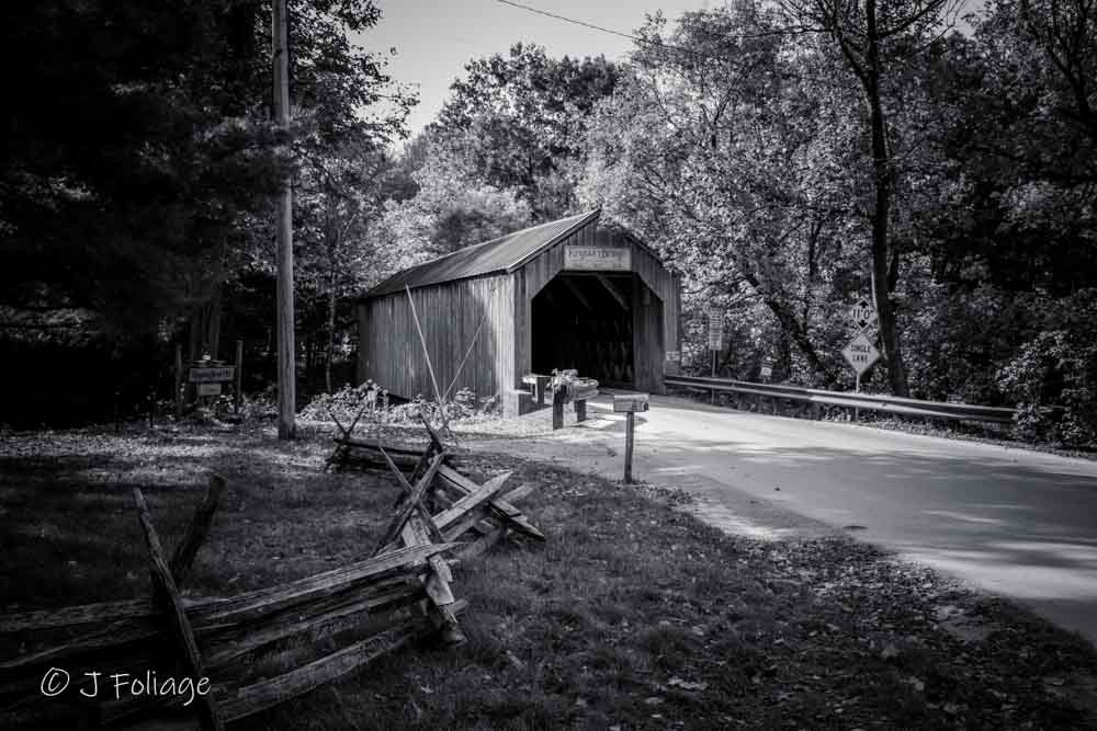 Black and white photograph of Kingsley Covered Bridge in Clarendon, Vermont, featuring late morning shadows on a dirt road.