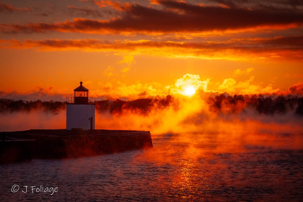 Golden hour sunlight backlighting heavy arctic sea fog at Derby Wharf Lighthouse in Salem MA