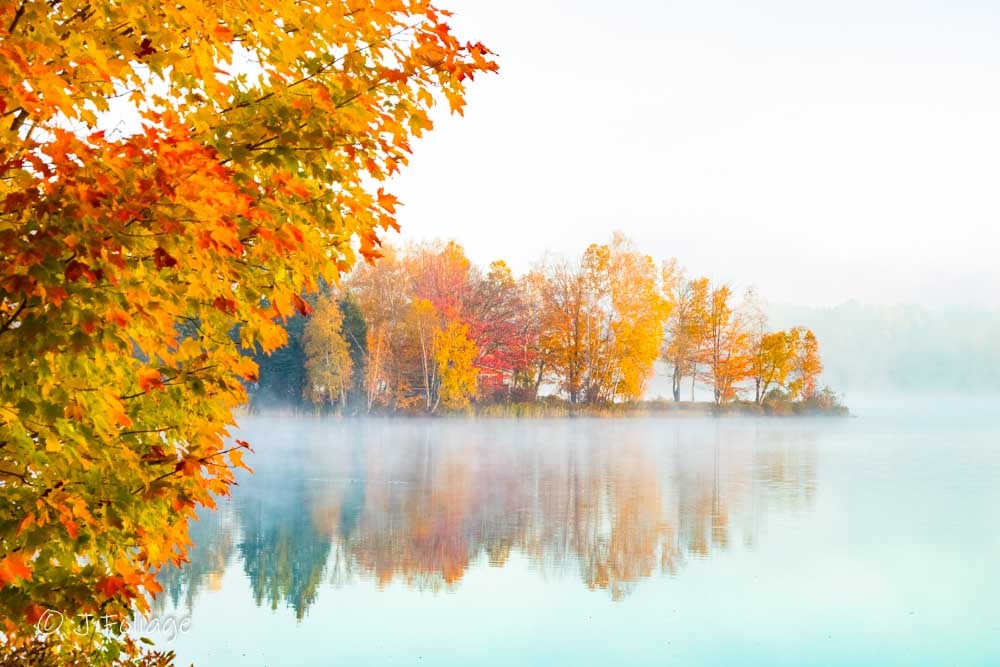 The New England fall colors of Maine glow through the fog in the early morning sunshine. Haley Pond is right next to Rangeley Lake Maine.