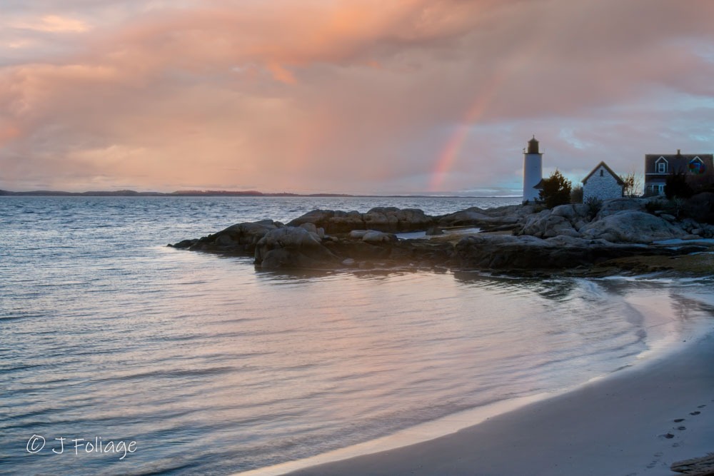 Serene coastal photography of Annisquam Lighthouse at sunset with a soft rainbow and misty horizon, creating a calming blue palette for residential interiors.