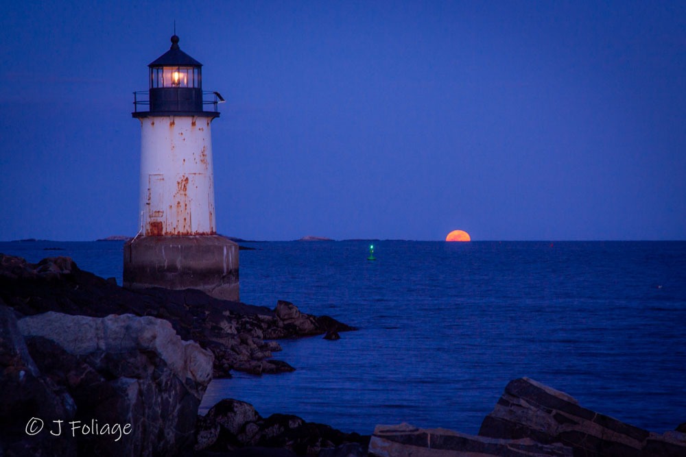 Full moon breaking the horizon past one of two of Salem's Lighthouses