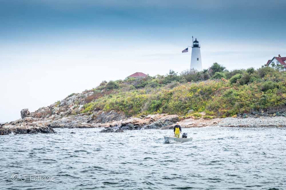 A lobsterman checking traps in a small boat near the Baker Island Lighthouse in Salem Massachusetts